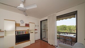A living room with a flat-screen TV, bookshelves, a sofa, and a balcony with a table and chairs. - Residence Riviera 43 by Wonderful Italy (Desenzano del Garda)