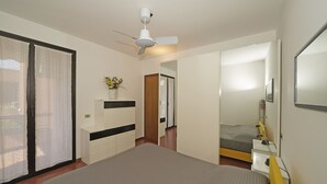 A bedroom with a bed, a bedside table with a lamp, a ceiling fan, and a sliding glass door leading to an outdoor area. - Residence Riviera 43 by Wonderful Italy (Desenzano del Garda)