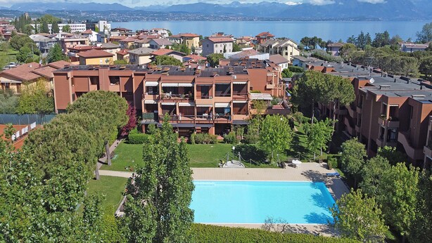 A hotel with a swimming pool surrounded by greenery, a view of a lake, and mountains in the background. - Residence Riviera 43 by Wonderful Italy (Desenzano del Garda)