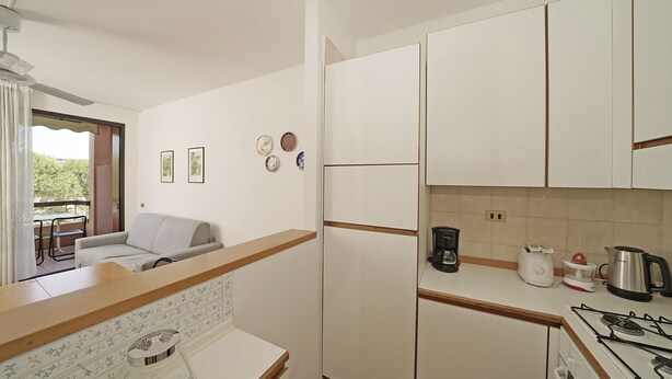 Cocina compacta con gabinetes blancos, una encimera, estufa a gas, cafetera y tostadora.