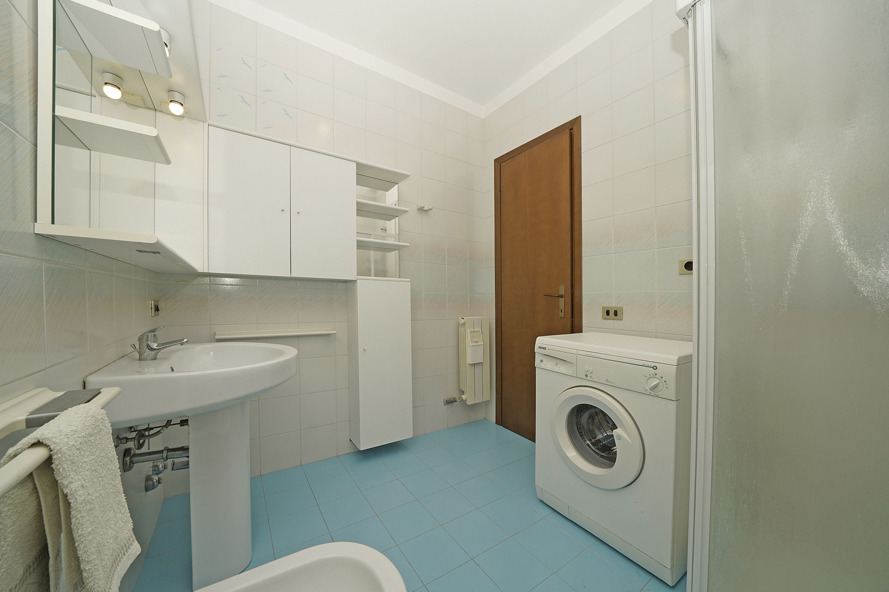 A bathroom with a sink, mirror, towel rack, and a washing machine.
