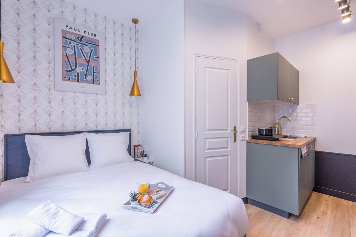 A hotel room with a neatly made bed, a small kitchenette, and a wall-mounted artwork.