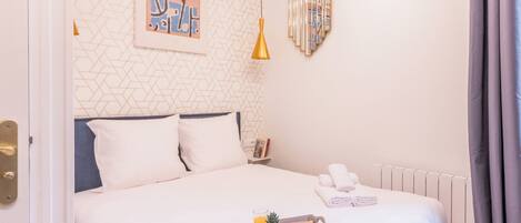 Una cama bien hecha con ropa blanca, una bandeja con alimentos para el desayuno y una pared con patrones geométricos y una obra de arte enmarcada.
