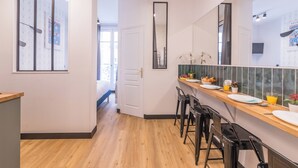 A modern kitchen with a wooden countertop, bar stools, and a view into the adjacent bedroom. - WS Champs-Elysées - Colomb (Paris)