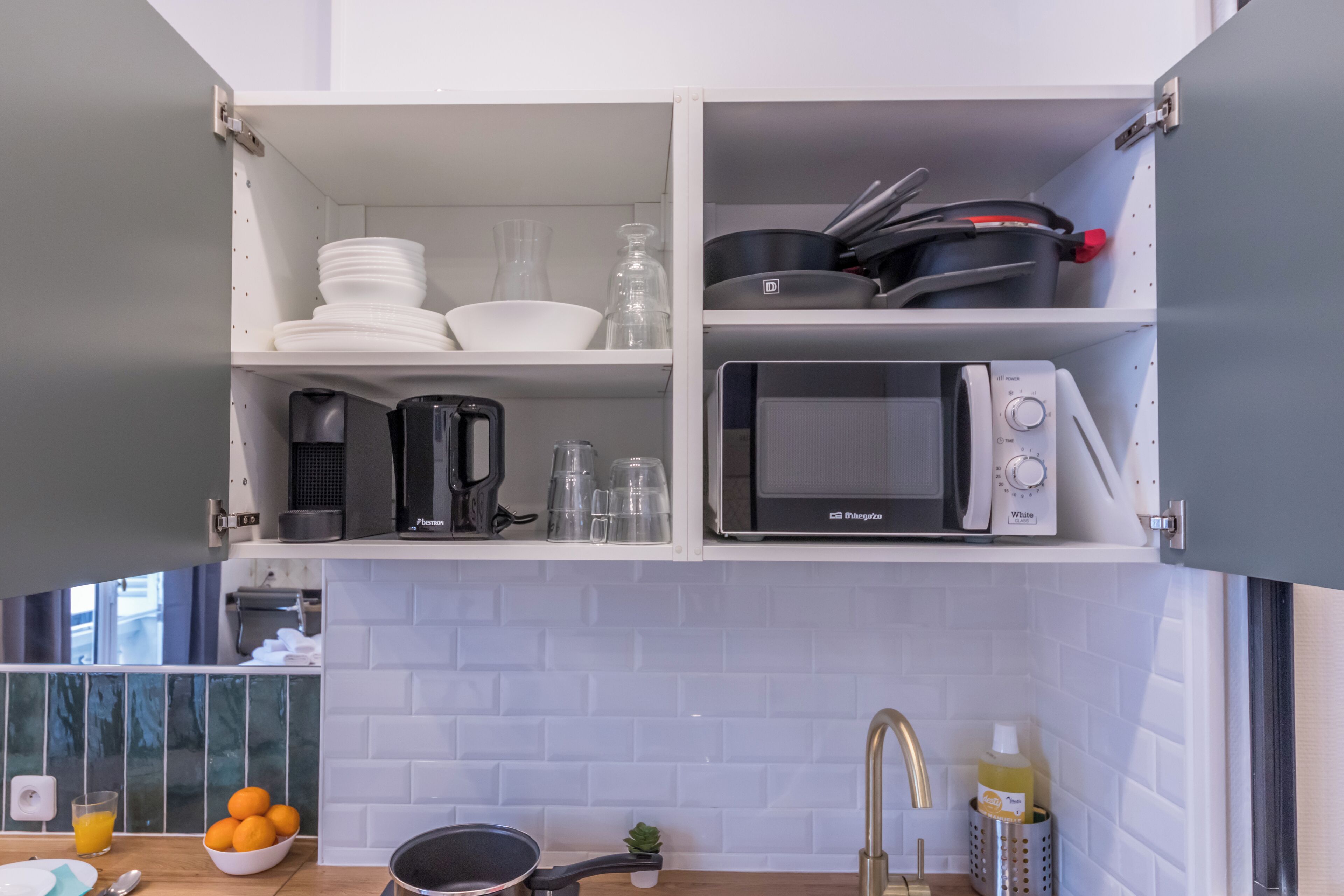 A kitchen with white cabinets, a microwave, a kettle, and a sink.