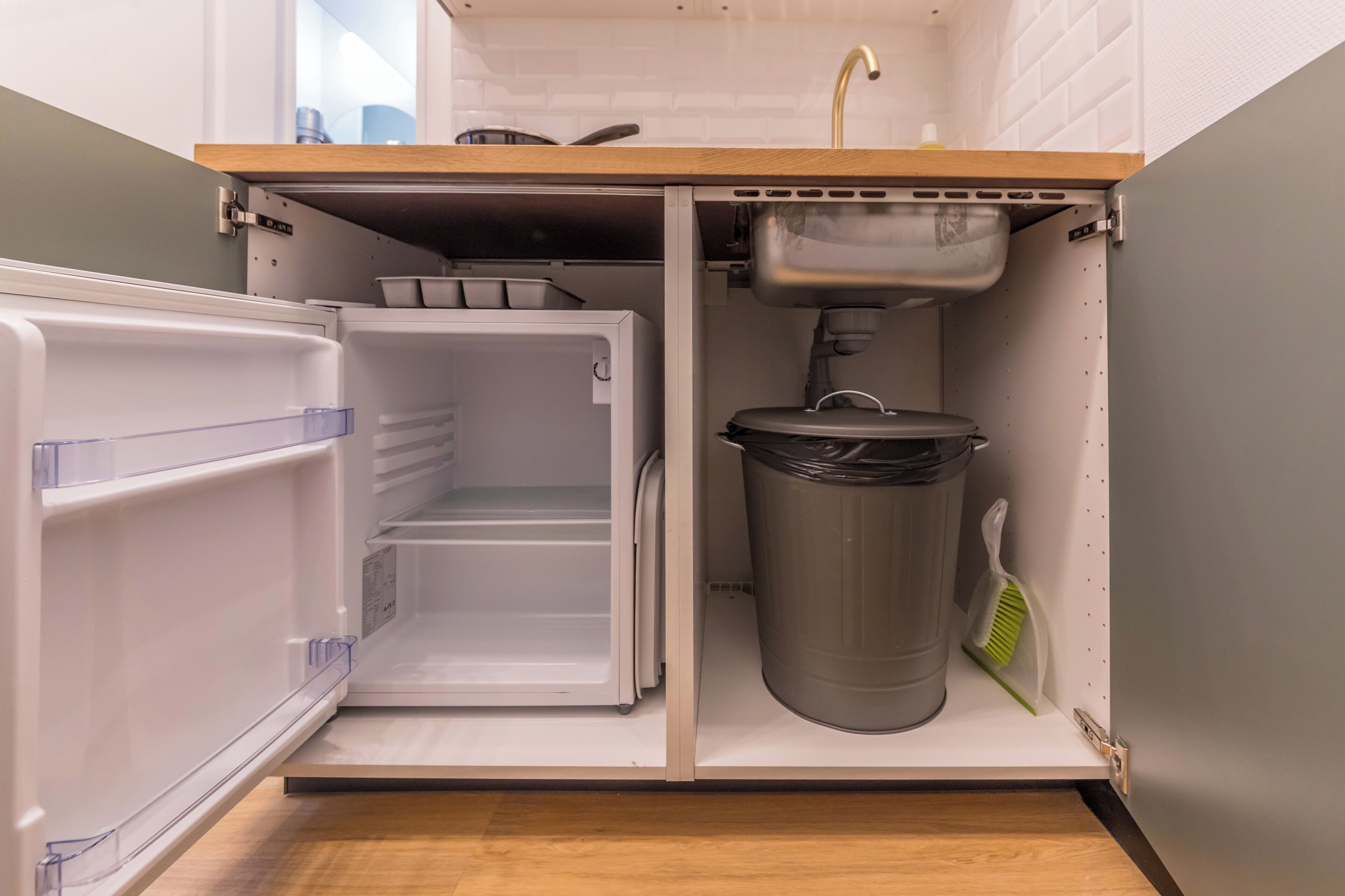 A compact kitchen with a built-in refrigerator, a sink, and a trash bin.