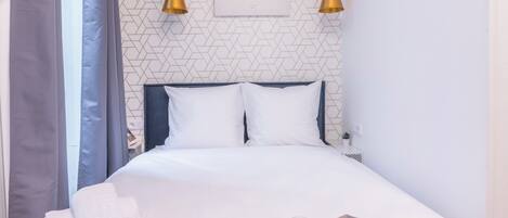 A neatly made bed with pillows, a tray with orange juice and a muffin, and a framed artwork on the wall.