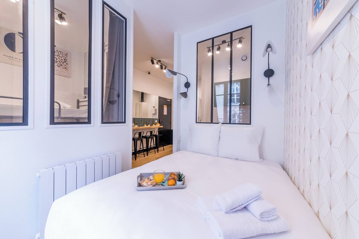 A modern hotel room with a large bed, a tray of breakfast, and a view into the kitchen area.