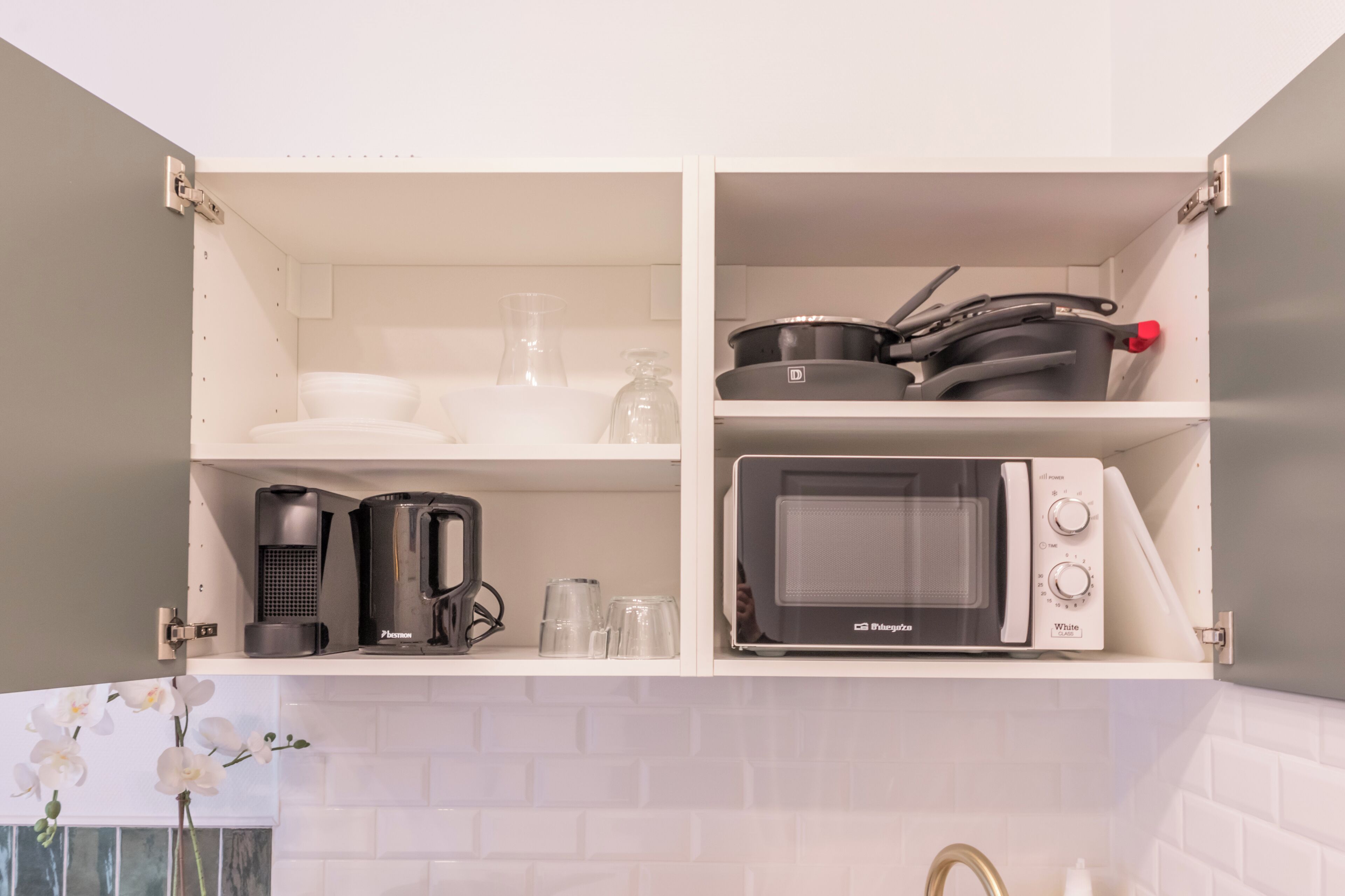 A kitchen with white cabinets, a microwave, a coffee maker, and a glass carafe.