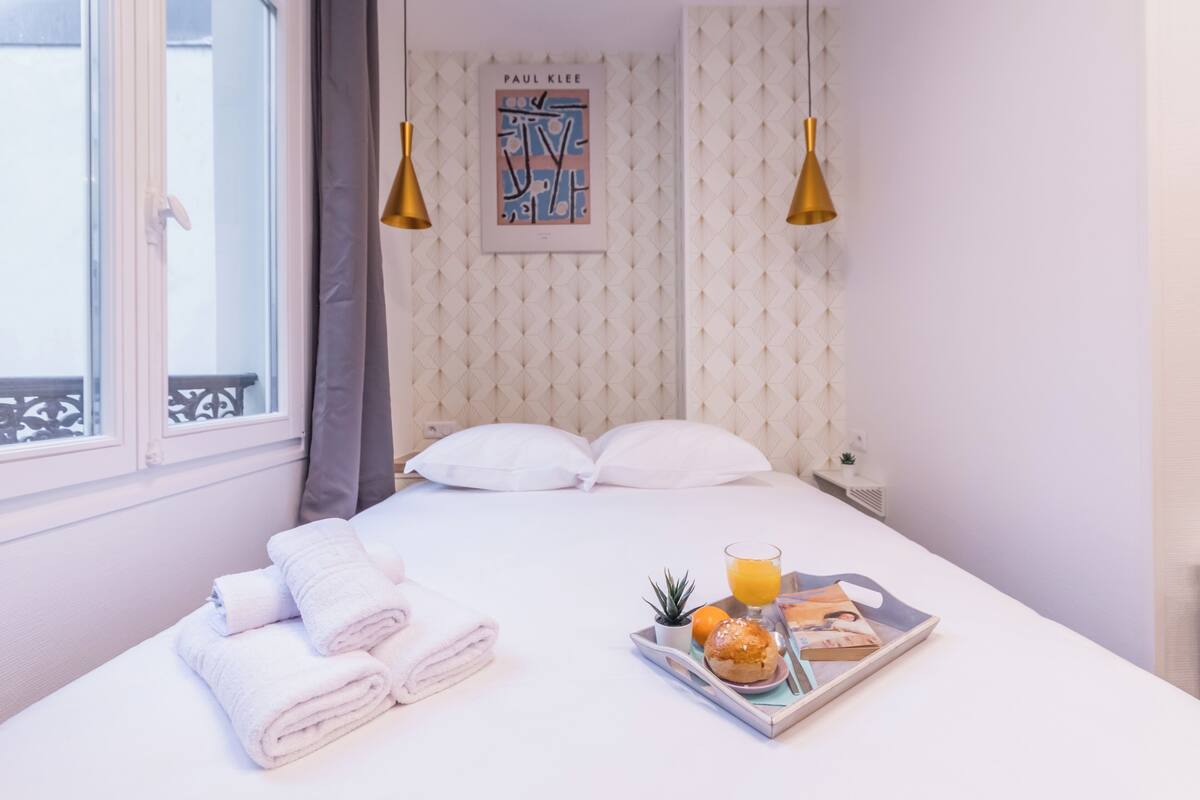 A neatly made bed with white linens, a tray with breakfast items, and a framed artwork on the wall.