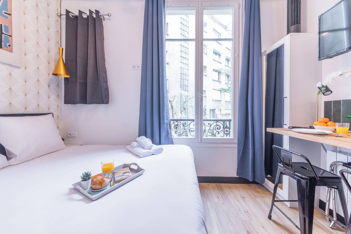 A hotel room with a bed, breakfast tray, and a window with curtains.