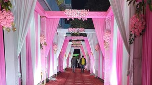 A corridor with pink and white drapes, floral decorations, and a patterned carpet. - Hotel Vibrant Lawn And Banquet (Danapur)