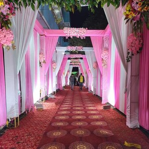 A corridor with pink and white drapes, floral decorations, and a patterned carpet.