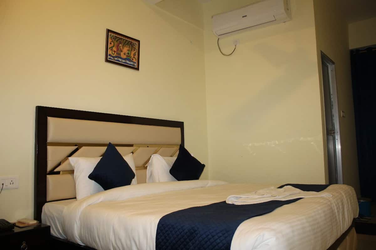 Une chambre d’hôtel avec un lit, une table de chevet, un climatiseur fixé au mur et une porte.