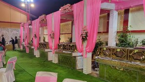 An outdoor event space with green artificial grass, pink draped curtains, and floral arrangements. - Hotel Vibrant Lawn And Banquet (Danapur)