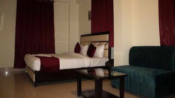A hotel room with a bed, a sofa, a coffee table, and a nightstand. - Hotel Vibrant Lawn And Banquet (Danapur)