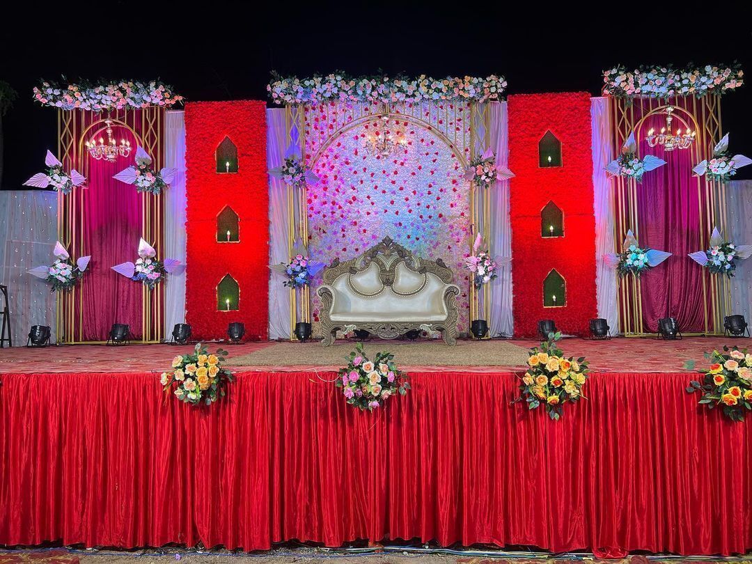 Un escenario con un telón rojo, un sofá blanco y decoraciones florales.