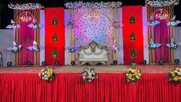 Un escenario con un telón rojo, un sofá blanco y decoraciones florales.