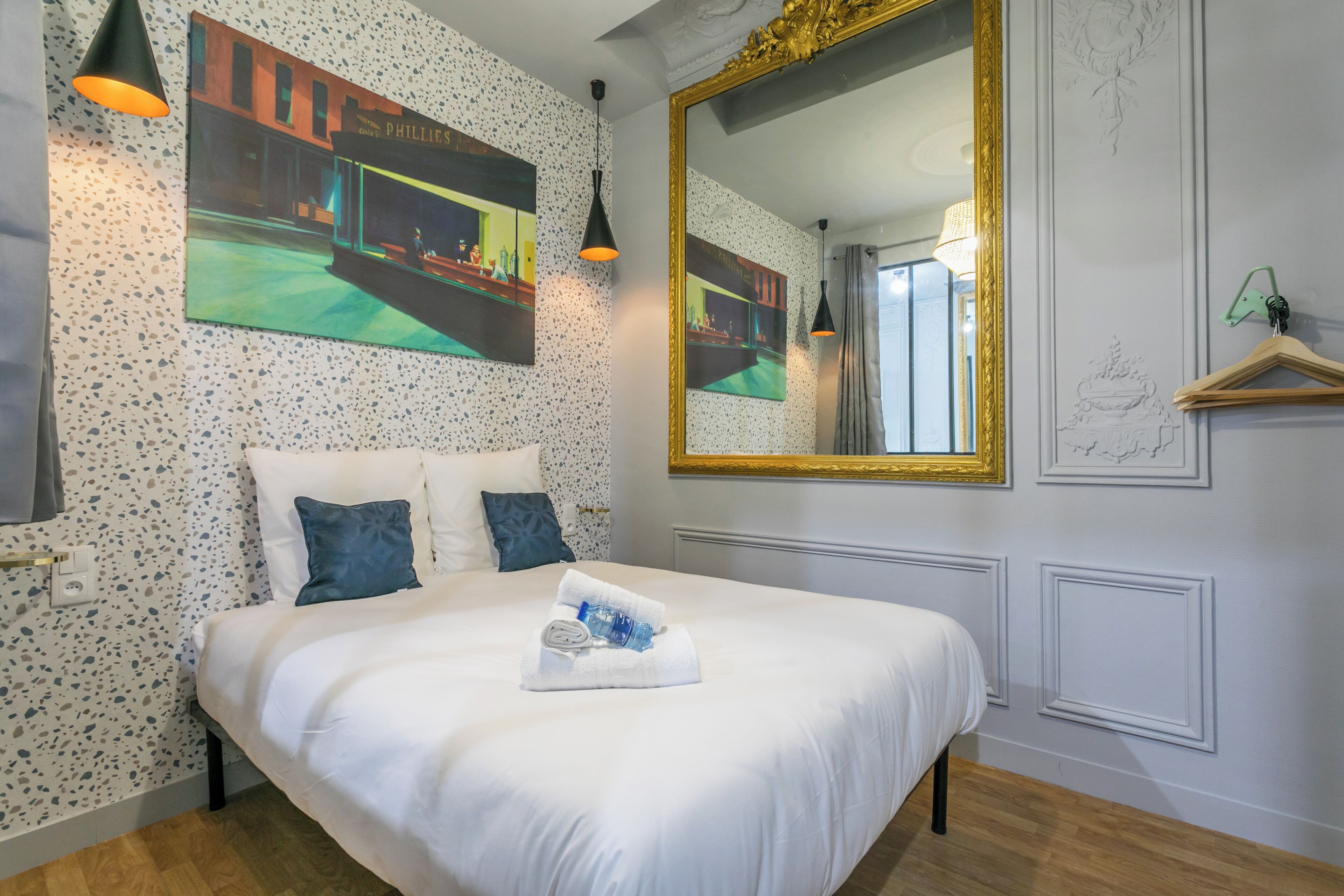 Una habitación de hotel con una cama, un espejo grande y obras de arte en las paredes.