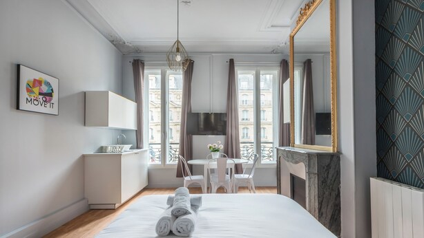 A hotel room with a bed, a desk, a chair, a mirror, and a window with curtains. - WS Saint-Lazare - Opera (Paris)