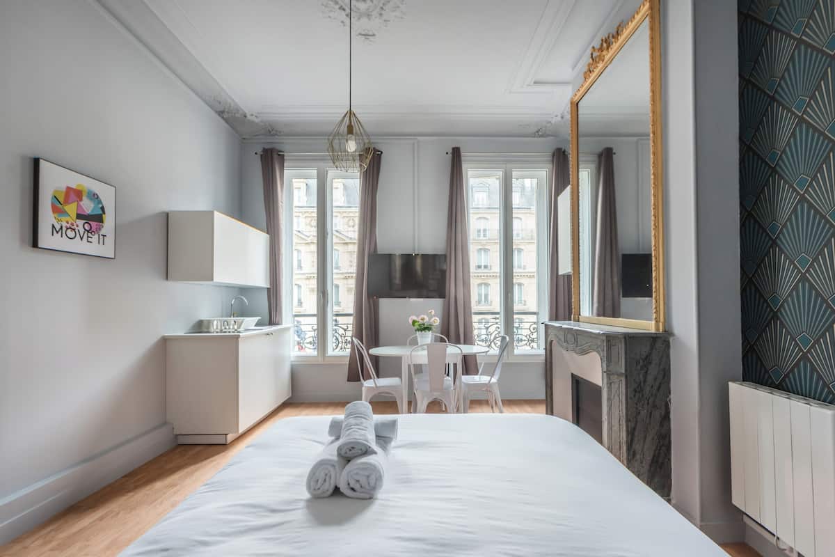 Une chambre d’hôtel avec un lit, un bureau, une chaise, un miroir et une fenêtre avec des rideaux.