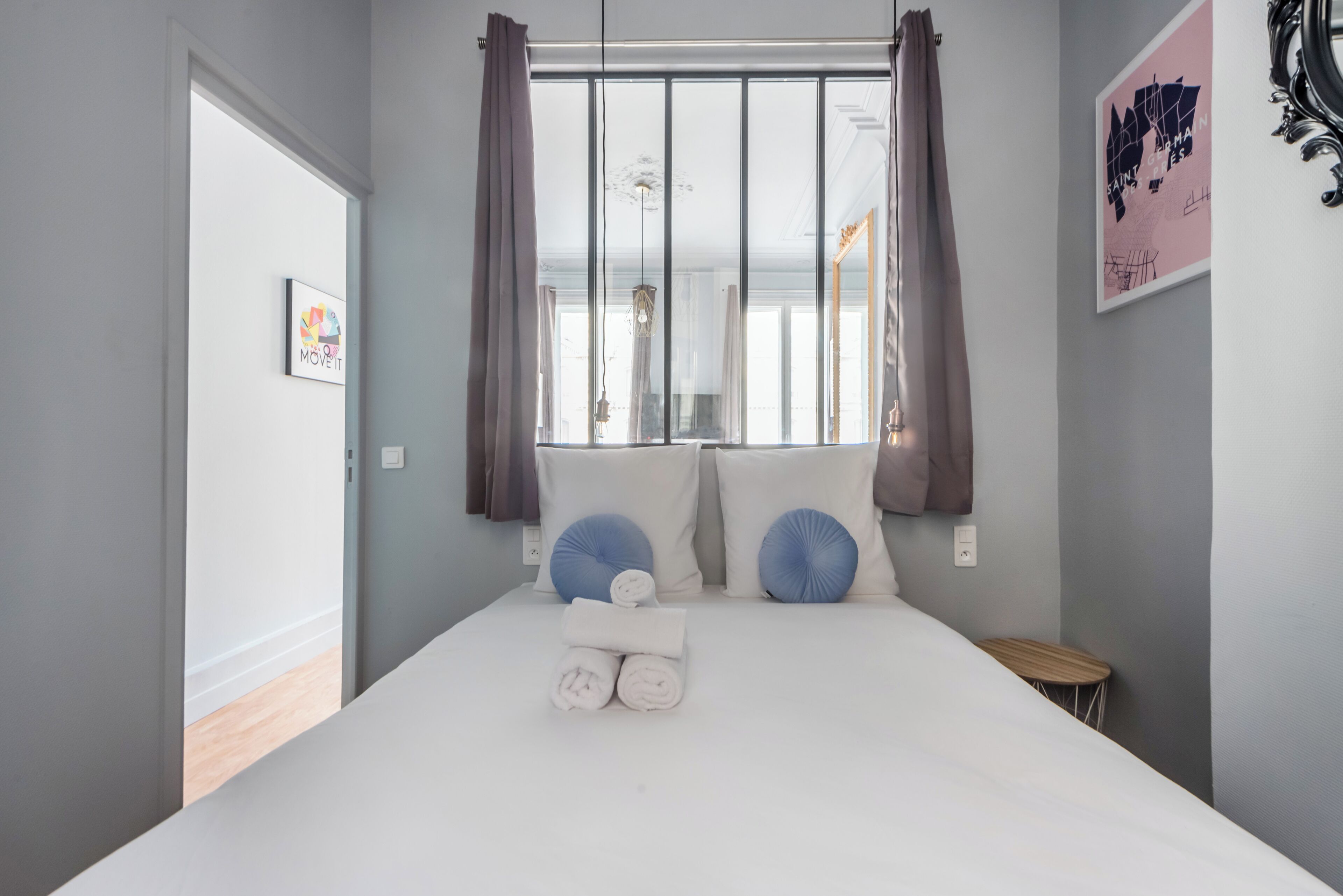 A bedroom with a bed, pillows, a small table, and a window with curtains.