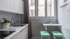 A modern kitchen with white cabinets, a stainless steel sink, a window with a view of buildings, and a small window seat with a plant. - WS Saint-Lazare - Opera (Paris)