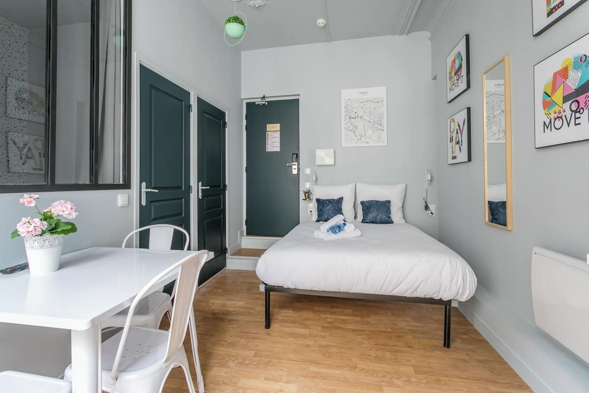 Une chambre à coucher avec un lit, un bureau blanc et des chaises. Une porte donne accès à une autre pièce.