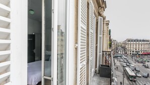 A room with a bed, a glass door, and a view of a busy street with buildings and vehicles. - WS Saint-Lazare - Opera (Paris)