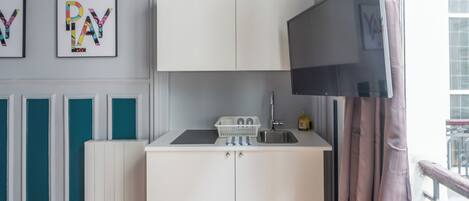 A modern kitchen with white cabinetry, a built-in sink, and a flat-screen TV mounted above the counter.