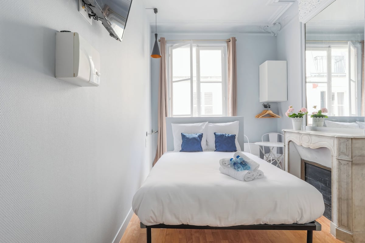 Une chambre d’hôtel moderne avec un grand lit, une cheminée, une fenêtre avec des rideaux, un luminaire suspendu et une petite table avec une chaise.