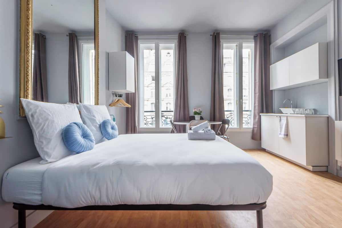 Une chambre d’hôtel moderne dotée d’un grand lit, d’un petit coin repas et offrant une vue sur la ville grâce à de grandes fenêtres.