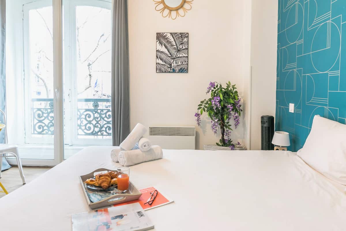 A hotel room with a bed, a tray of croissants and juice, a magazine, and a vase with flowers.