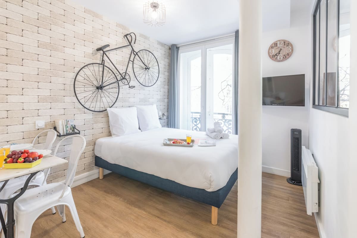 A modern bedroom with a brick wall, a bicycle, a bed, a TV, and a breakfast setup.