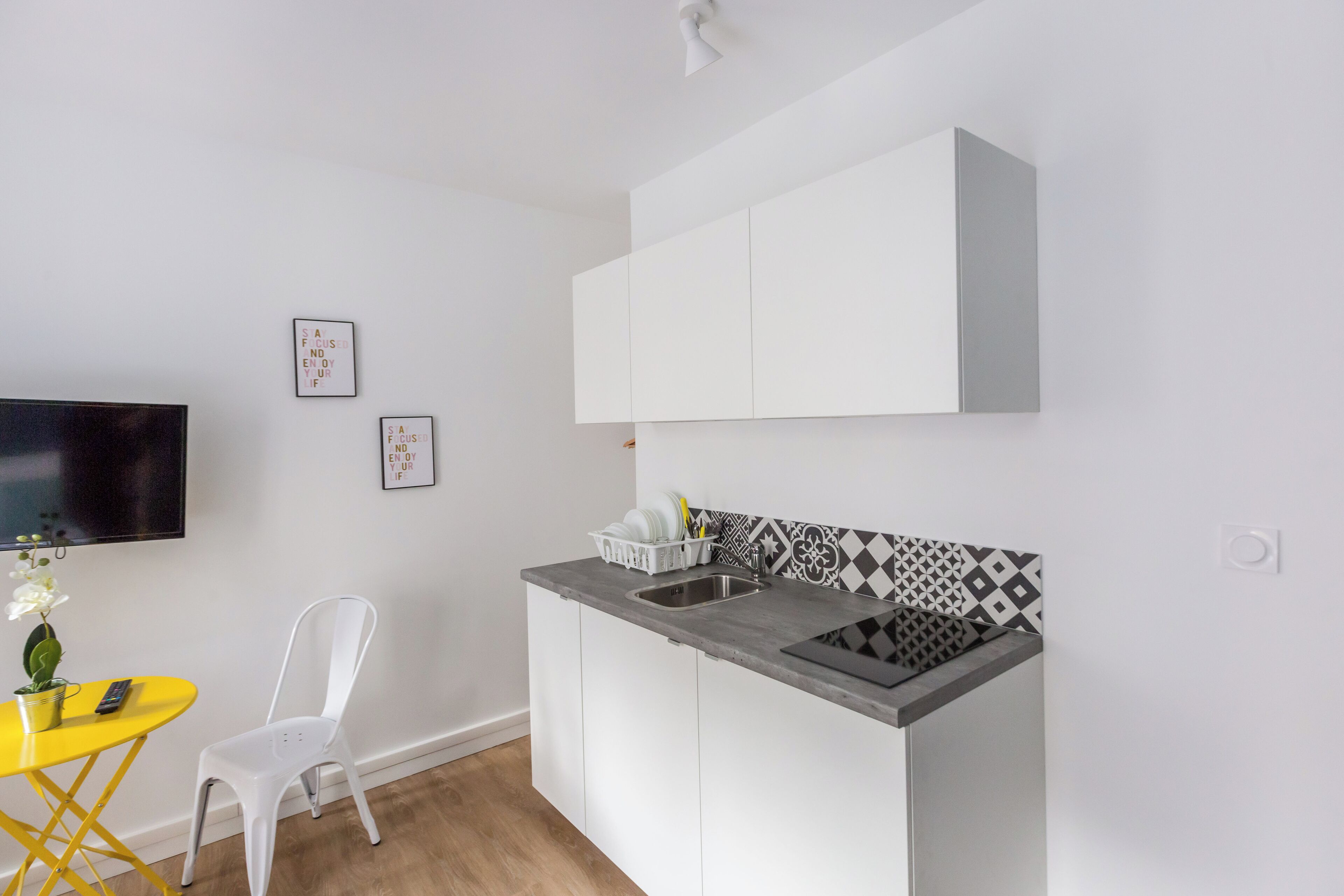 Una cocina compacta con armarios blancos, encimera gris, un lavamanos pequeño y salpicadero de azulejos.