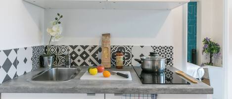 Una cocina con un fregadero, una tabla de cortar con verduras, un cuchillo, una olla y una cuchara de madera.