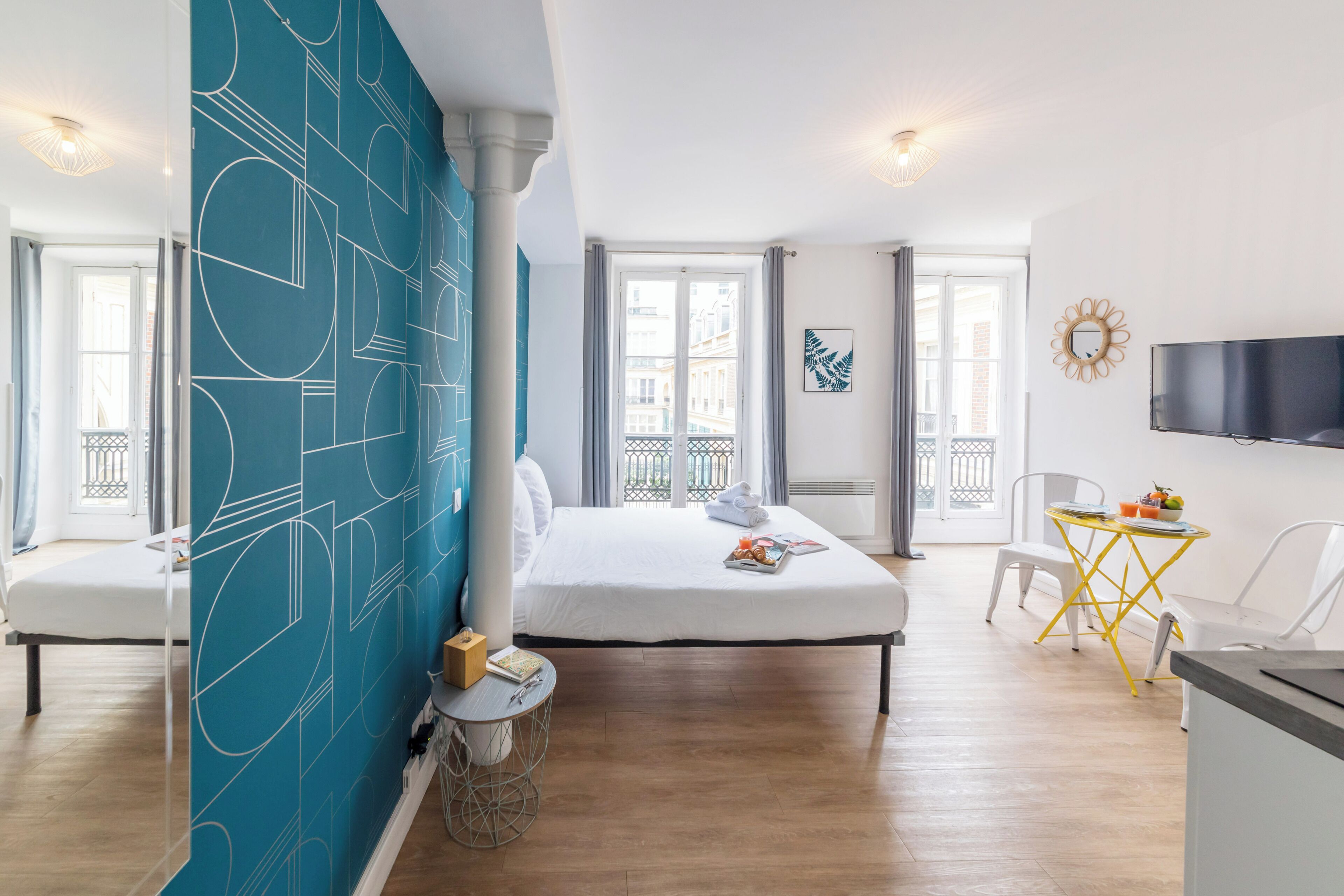 Hotelkamer met een groot bed, een klein tafeltje met stoel, een aan de muur bevestigde televisie en een balkon met uitzicht op de stad.