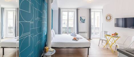 Hotelkamer met een groot bed, een klein tafeltje met stoel, een aan de muur bevestigde televisie en een balkon met uitzicht op de stad.