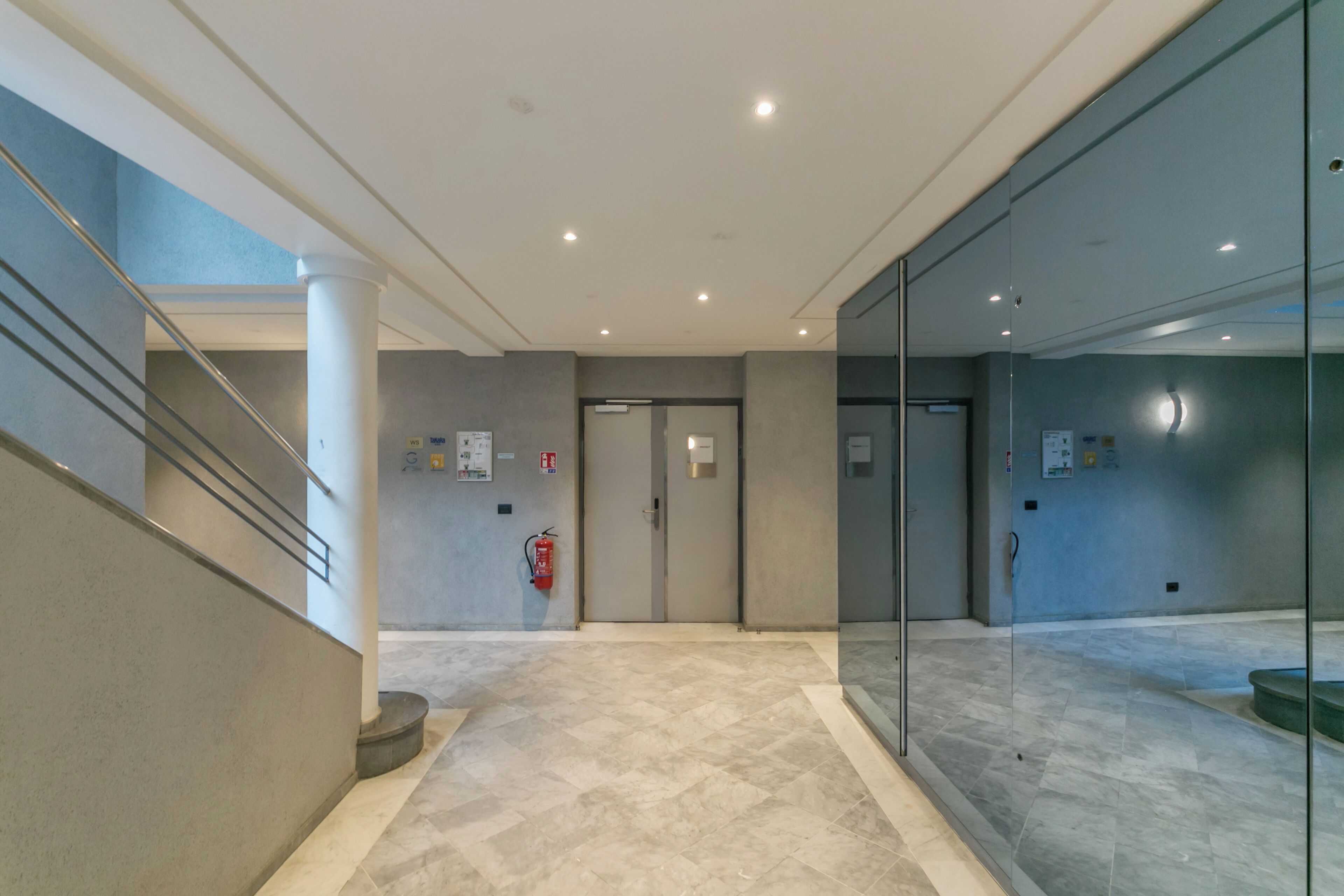 A modern hallway with a marble floor, glass walls, and a staircase.