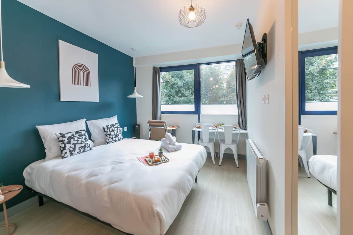 A modern bedroom with a large bed, a desk, and a chair, a radiator, and a TV on the wall.