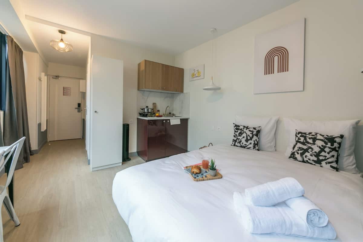 A hotel room with a bed, a small kitchenette, and a bathroom.