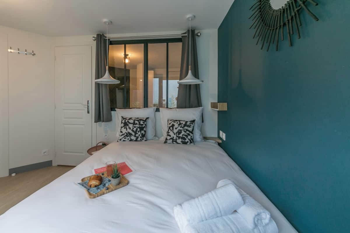 A neatly made bed with a tray of breakfast items, a bedside table, and a wall-mounted light fixture.