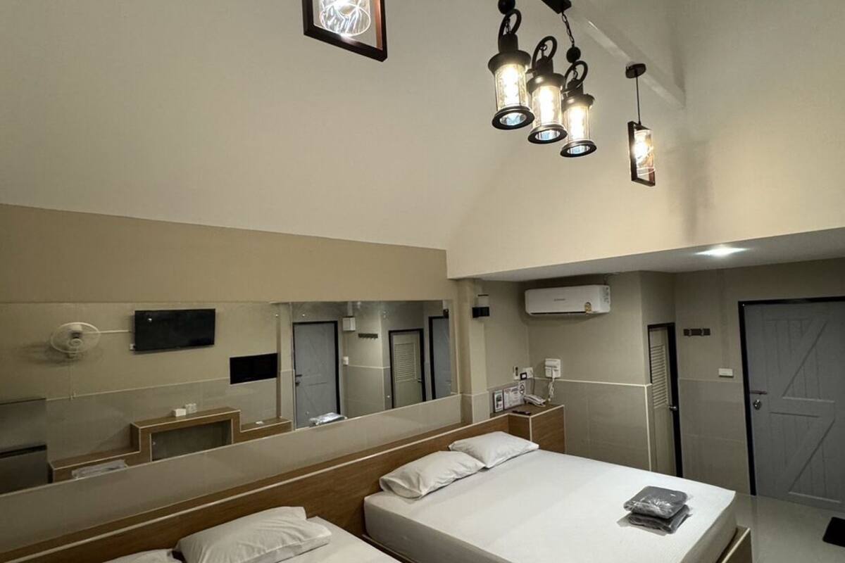 A hotel room with two beds, a large mirror, a TV, and a ceiling light fixture.