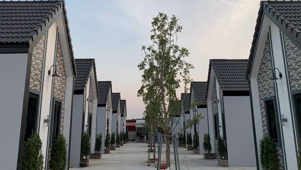 A row of modern buildings with a central walkway, each with a stone facade and tiled roofs.