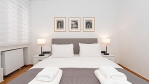 A neatly arranged hotel room with a large bed, two bedside tables with lamps, a radiator, and three framed pictures on the wall.