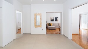 A spacious, modern living area with a neutral color palette, a wooden-framed mirror, and a sofa with cushions.