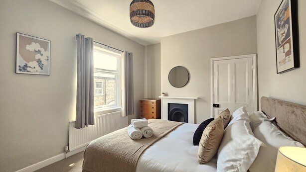 Un dormitorio con cama, cómoda, espejo, chimenea y ventana.