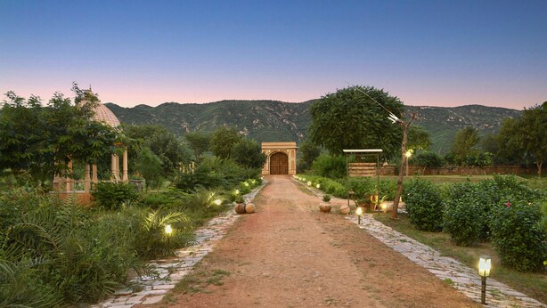 A pathway leading to a building with a dome and an archway, surrounded by greenery and stone paving.
