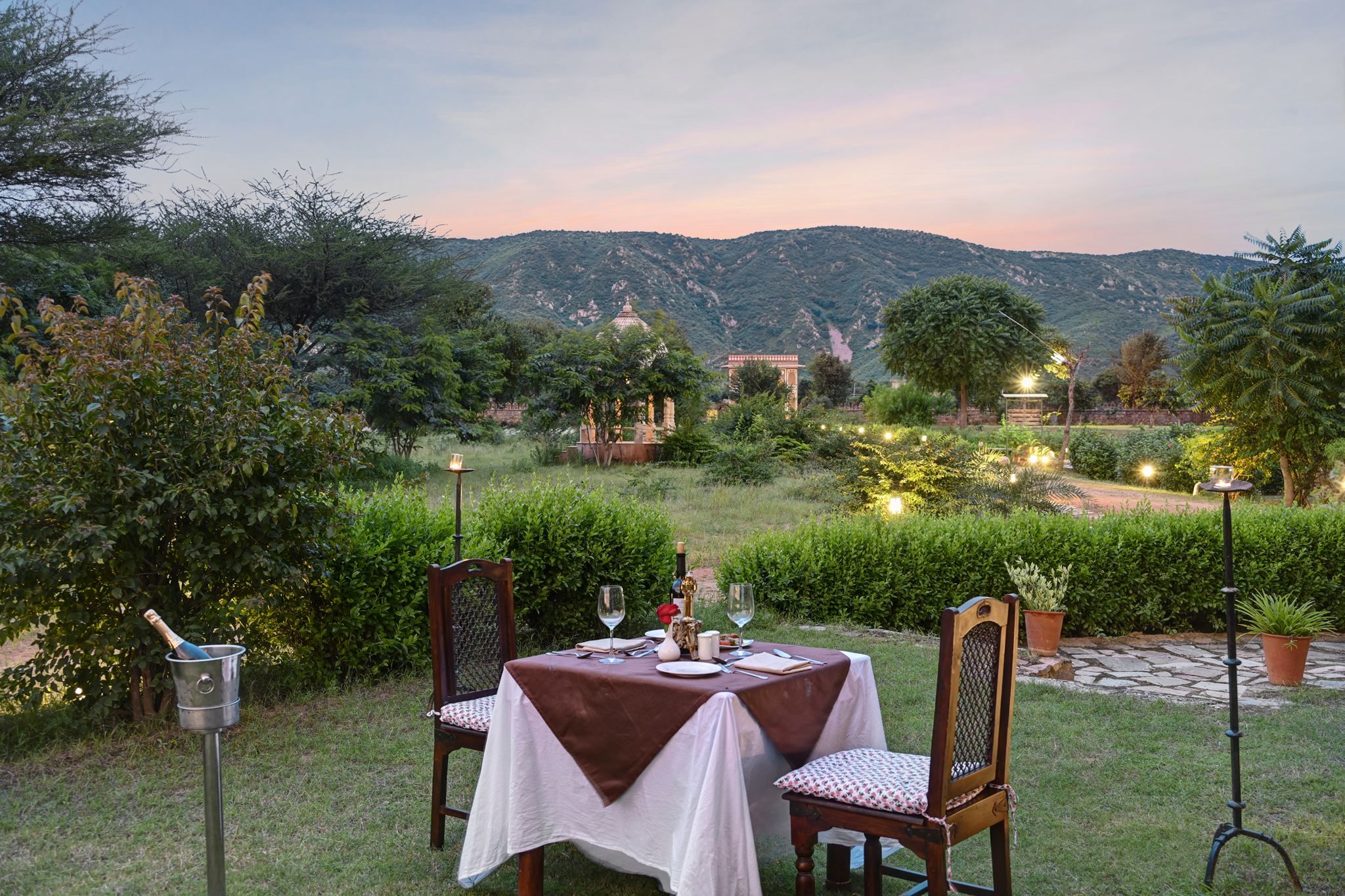 Un espace de restauration en plein air avec une table dressée pour deux personnes, entouré de verdure et avec une chaîne de montagnes en toile de fond.