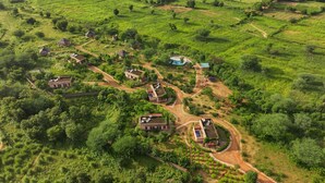 An aerial view of a rural village with several houses, pathways, and a small pond.